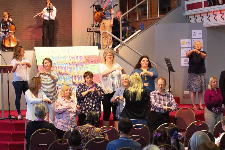 The B2gether group at Upton Vale Baptist Church leading a Disability Awareness Sunday service in 2022. The group are signing in Makaton; musicians are playing in the background.